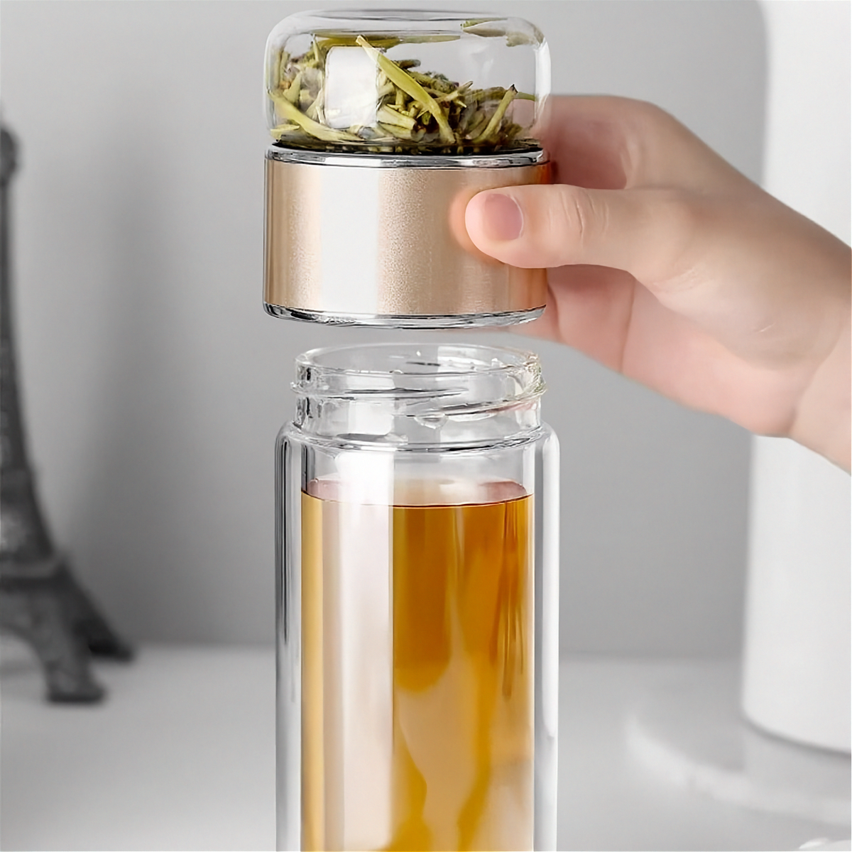 Gourde en verre avec infuseur TEVA 390 ml — compartiment à thé doré soulevé au-dessus de la gourde.
