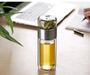 Gourde en verre avec infuseur TEVA 390 ml — remplie de thé sur un bureau près d’un ordinateur.