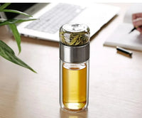 Gourde en verre avec infuseur TEVA 390 ml — remplie de thé sur un bureau près d’un ordinateur.