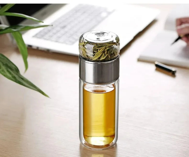 Gourde en verre avec infuseur TEVA 390 ml — remplie de thé sur un bureau près d’un ordinateur.
