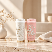 Gourde isotherme AURYN 500 ml — versions blanche et rose à fleurs avec bouchons fermés sur un socle en pierre.