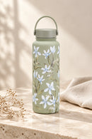 Gourde isotherme FLORA 1 L — vert sauge à fleurs blanches dans un décor intérieur.